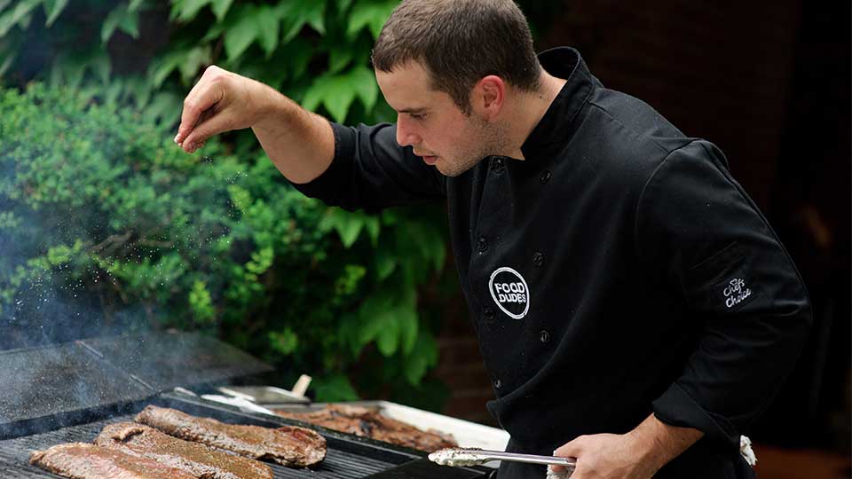 A Chef from The Food Dudes sprinkles salt on some steak
